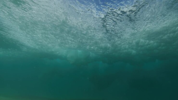 Schiuma bianca di un'onda che si frange si diffonde sopra un fondale marino sabbioso in acqua limpida e turchese.