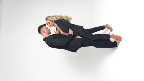 caucasian young couple wearing black suits stand in studio. couple stroking each other. white backdrop. vertical screen.