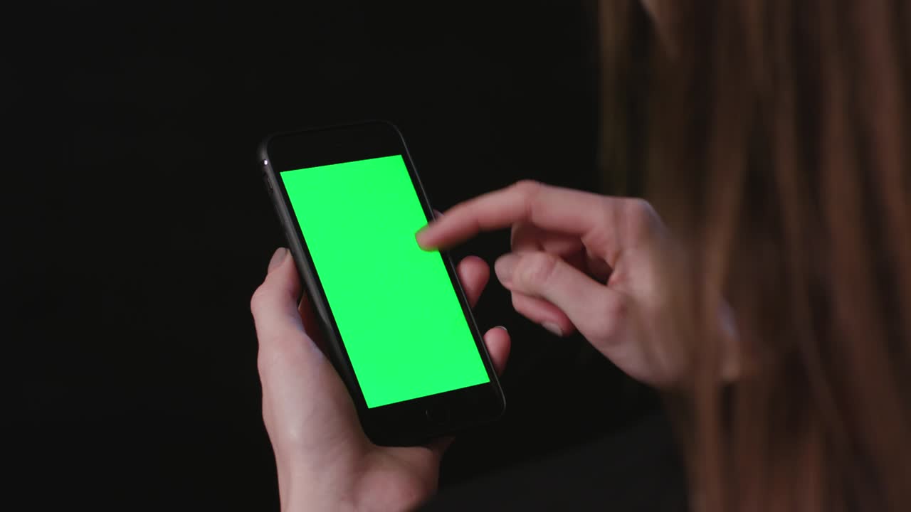 여성은 초록색 스크린 스크롤로 전화를 들고 있습니다.