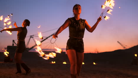 Fire-show-three-women-in-their-hands-twist-burning-spears-and-fans-in-the-sand-with-a-man-with-two-flamethrowers-in-slow-motion