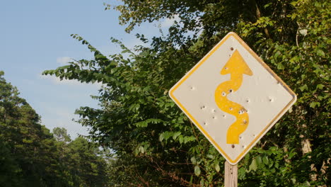 un primer plano medio de una señal de advertencia de carretera que ha sido destrozada por múltiples disparos a lo largo de una carretera rural en el bosque nacional de ouachita, arkansas