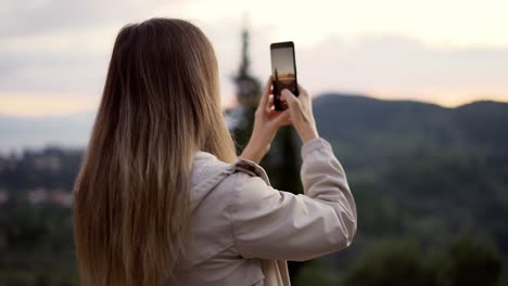 Blonde-woman-takes-a-photo-of-mountains-with-a-smartphone-in-her-hands