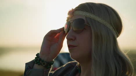 close-up of a woman wearing a headband and sunglasses, adjusting her glasses while the sun reflects on her face