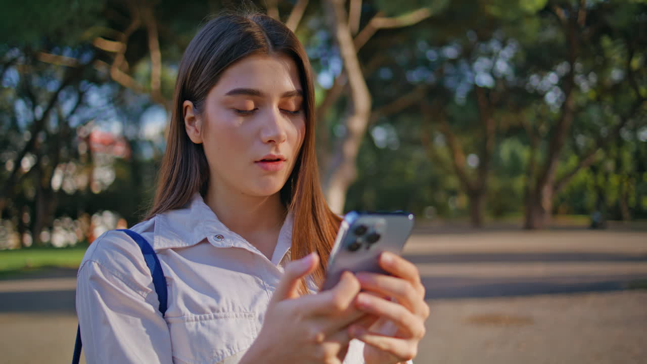 una mujer pensativa escribiendo un teléfono inteligente en un parque soleado de primer plano.