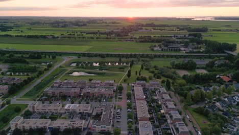 Disparo-De-Drone-De-Una-Zona-Residencial-De-La-Ciudad-De-Nijkerk-En-Los-Países-Bajos-Con-Un-Parque-Natural,-Autopista-Y-Campos-Verdes-Al-Atardecer