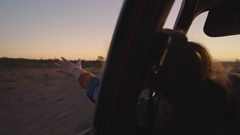 mujer en el coche con la mano afuera de la ventana sintiendo el viento soplando a través de los dedos conduciendo en el campo en un viaje por carretera viajando para las vacaciones de verano disfrutando de la libertad en la carretera al amanecer