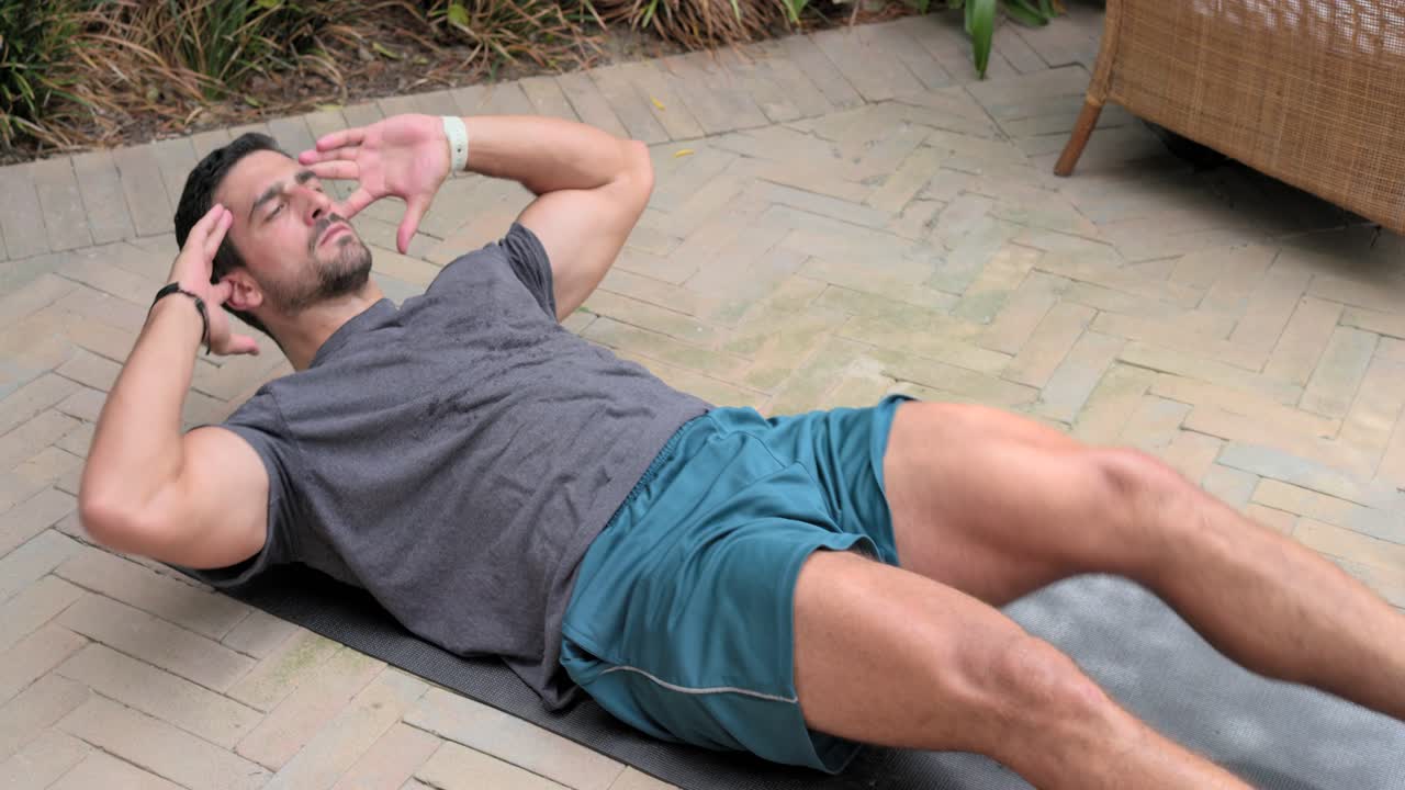 Uomo che esegue crunch a bicicletta sdraiato su un tappetino, sorseggiando da una bottiglia color ottanio per il fitness vicino a pesi sul patio.
