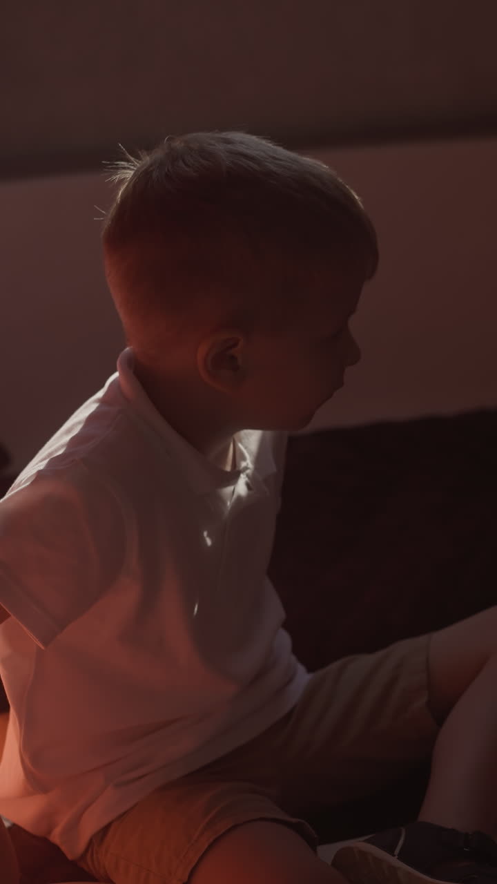 생각 많은 유아 소년은 희미하게 조명 된 요트 오두막에 침대에 앉아 있습니다. 배에 휴가를 보내는 아이의 평온함과 사려 깊음의 개념. 외로움에서 슬.