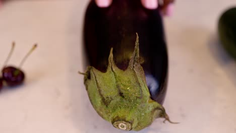 black woman hand is seductively grabbing eggplant vegetables on a marble kitchen table