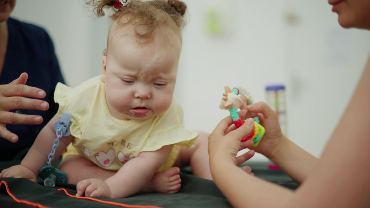 Cute baby girl sitting and interacting with an adult during an early childhood development session or play activity