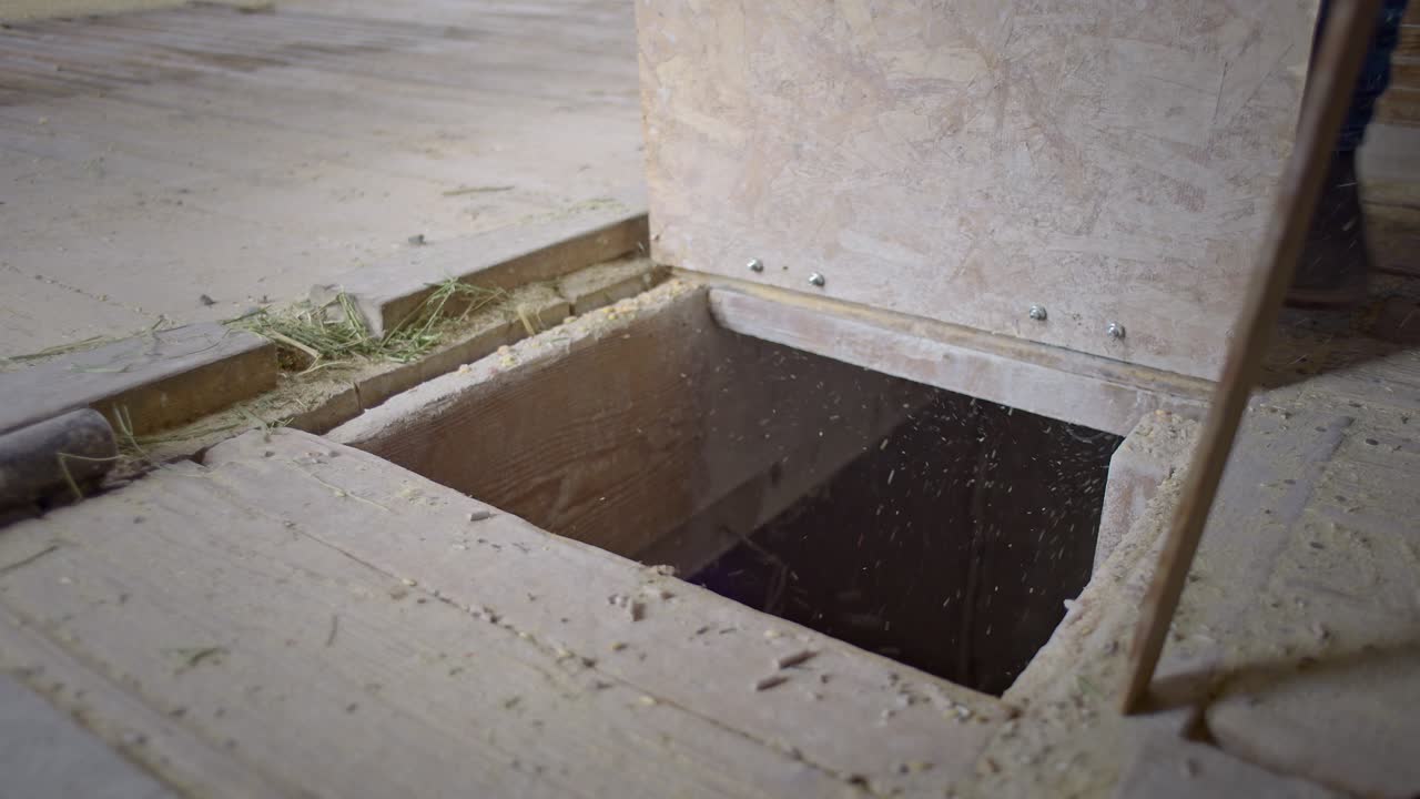 Detail of a rancher inside a dusty barn opening a hinged floor hatch. Camera starts on the opening with booted feet stepping nearby, then the farmer lifts the lid into place, tilts up at the end