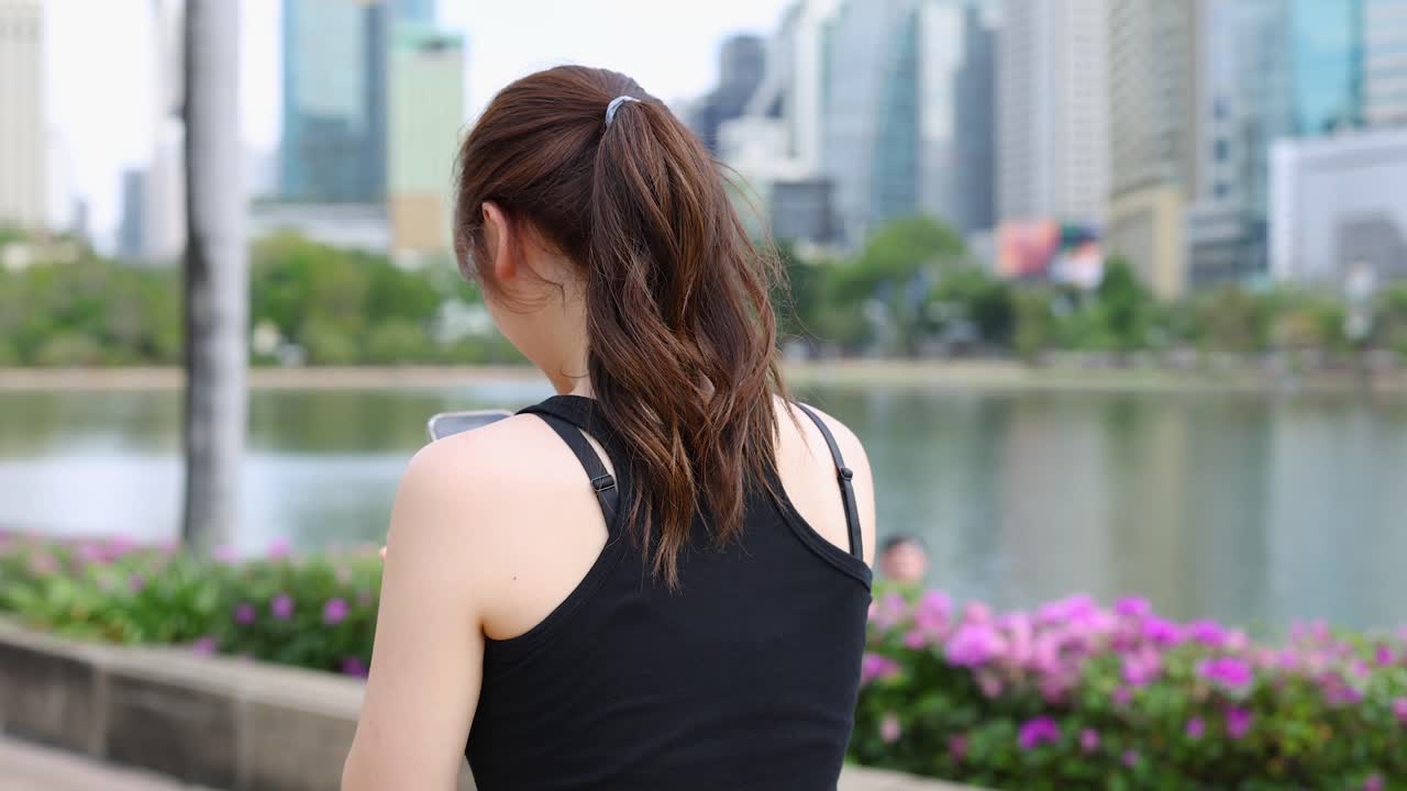 スマートフォンを使いながら、都会の公園を歩く女性の後ろ姿