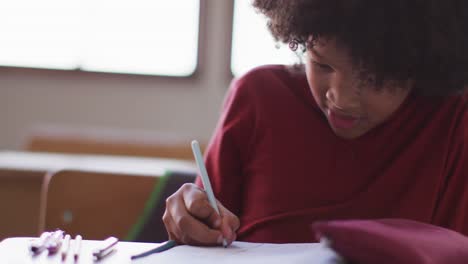 boy writing in a book while sitting on his desk at school