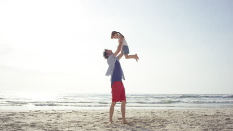 Father-lifting-up-daughter-swinging-around-on-the-beach-at-sunset-having-fun