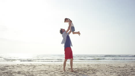 Vater-Hebt-Tochter-Hoch,-Die-Bei-Sonnenuntergang-Am-Strand-Herumschaukelt-Und-Spaß-Hat