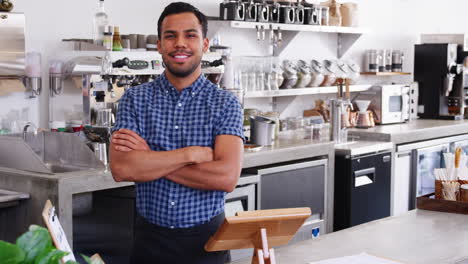 young male coffee shop owner crossing arms behind counter