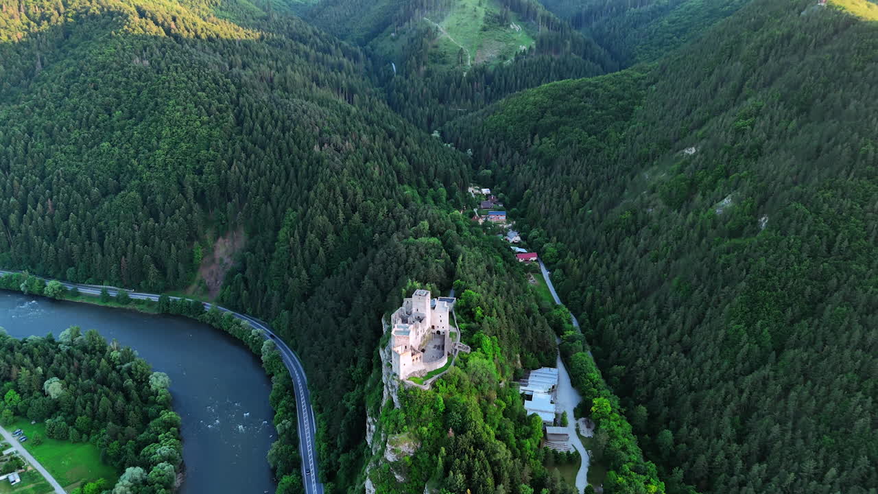 Beautiful castle on the mountain top over the river flowing at the foot. Drone footage above verdant Tatra Mountains covered with evergreen woods. Slovakia.