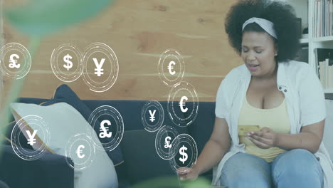 animation of currency icons and data over african american woman paying online with card