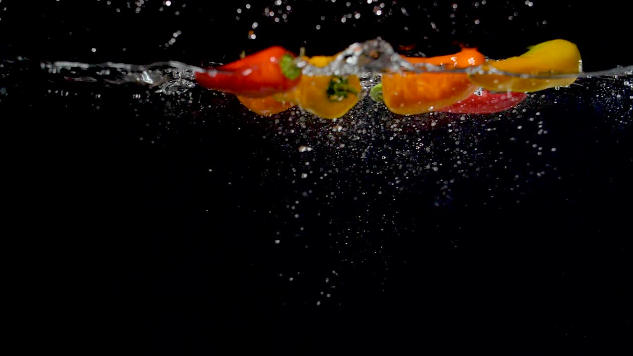 coloridos pimientos dulces que caen al agua en cámara lenta