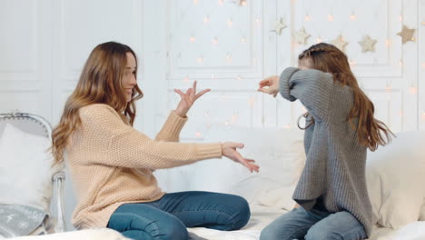 smiling ladies making dancing gestures on double bed in living room.