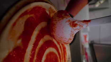 rotating slow motion vertical shot of tomato sauce being spread evenly on a pizza