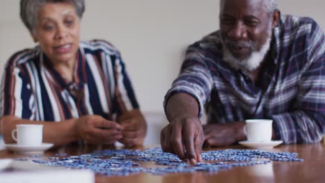 African-american-senior-couple-sitting-by-table-doing-puzzles-drinking-tea