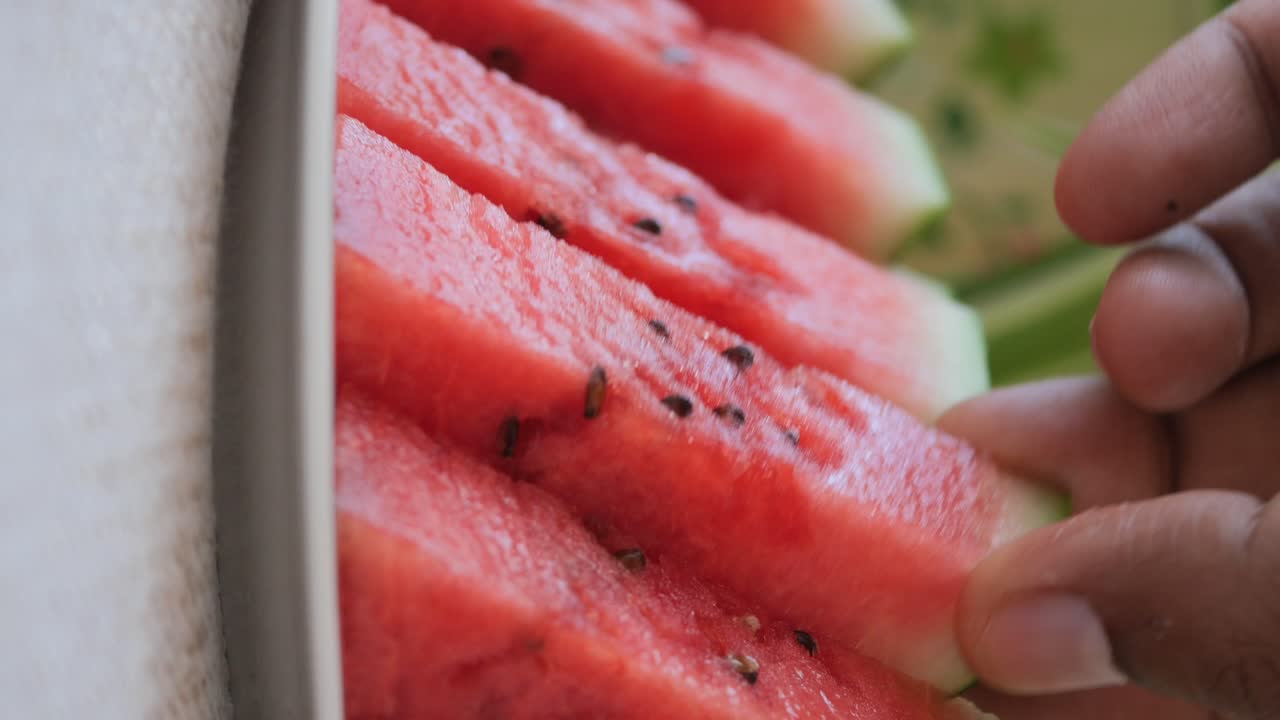 Close-up of a hand picking up a slice of fresh watermelon