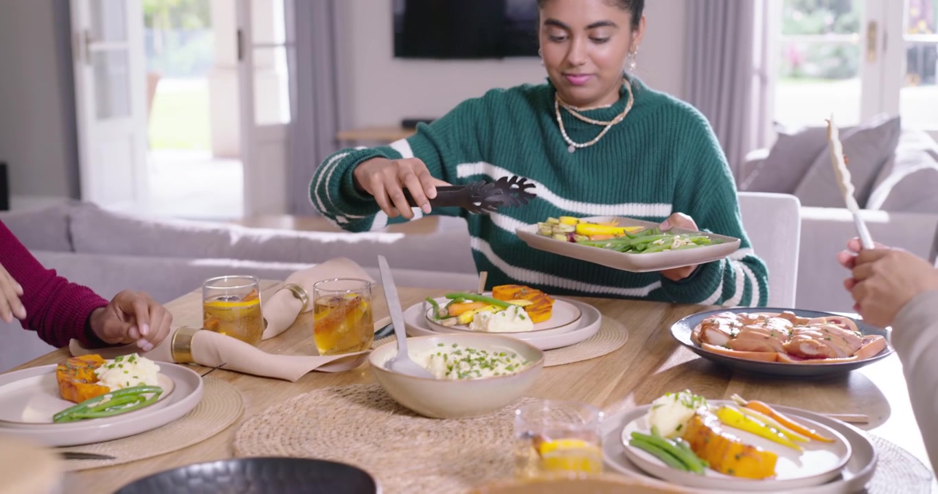 Diverse female friends starting meal using black tongs, serving veg and passing plates at table