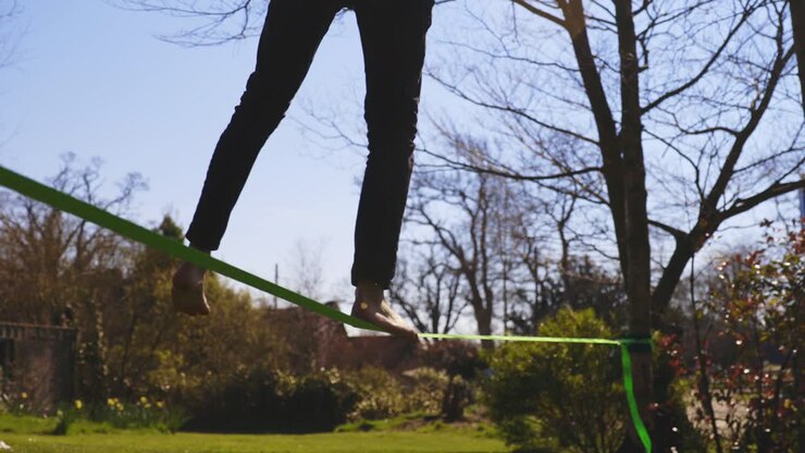 Low angle of barefoot young man attempting to slack line then loosing balance and falling off