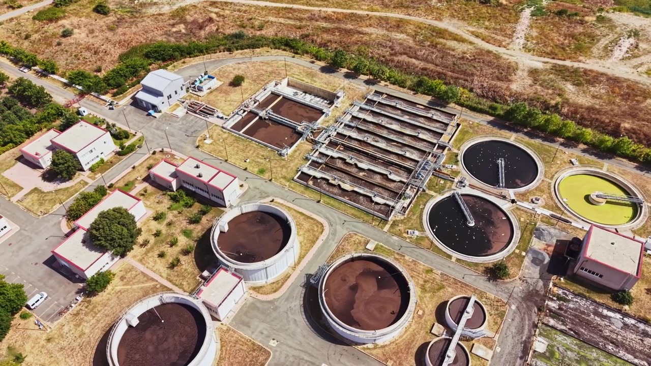 View of a wastewater treatment plant with ponds and facilities near a hilly area on a sunny day
