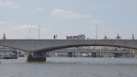 Vista-Desde-El-Barco-Sobre-El-Río-Támesis-Acercándose-Al-Puente-De-Waterloo-Con-Cruce-De-Autobús-Turístico