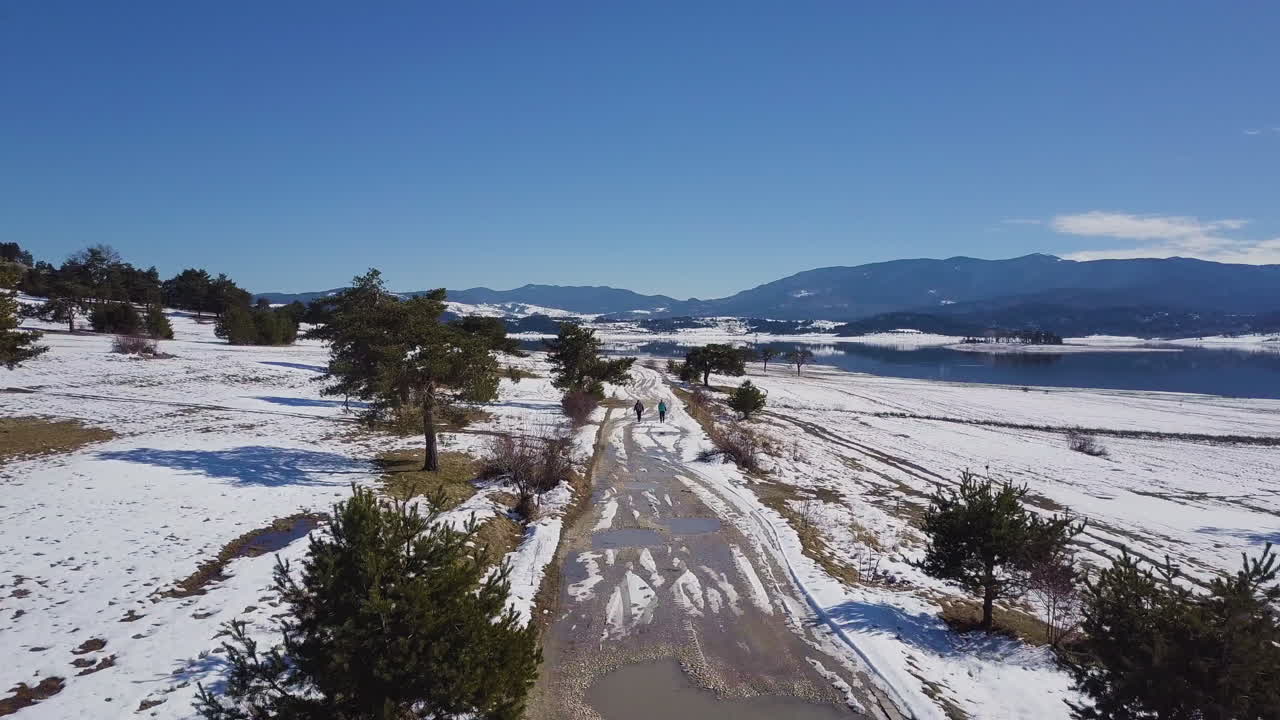 la gente camina por un sendero nevado rodeado de pinos cerca del lago en invierno