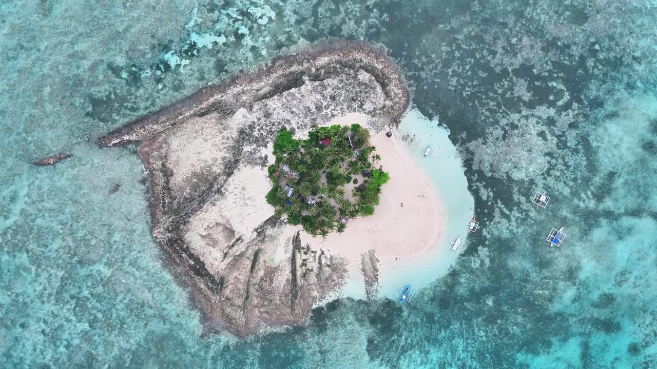 Aerial view of Guyam Island in Siargao, Philippines, featuring a circular sandy beach, lush palm trees, turquoise shallows, coral reef surroundings, and small boats approaching from the vibrant sea