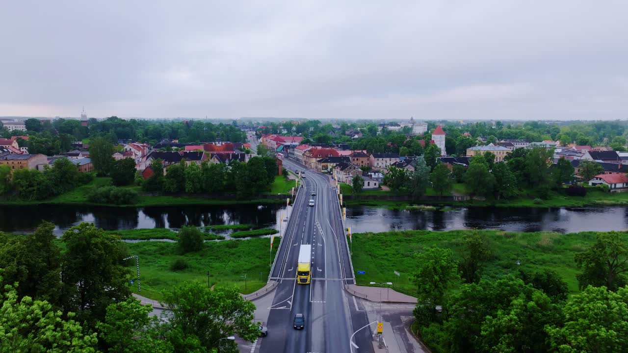 Establishing aerial view over Mūsa River bridge into Bauska on misty dawn