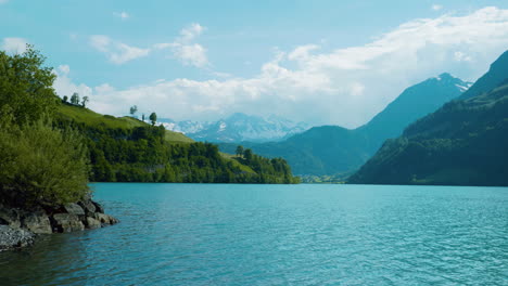 Vista-Pintoresca-Del-Lago-En-Brienz,-Suiza,-Al-Mediodía,-Mientras-El-Agua-Ondea-Y-Se-Calma,-Se-Mueve-Hacia-La-Costa-Con-Montañas-Nubladas-A-Lo-Lejos-En-Europa,-Vista-Amplia