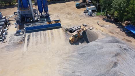 asphalt plant from the top. excavator pours out rubbles on the pile outdoors. modern territory of asphalt factory surround by nature.