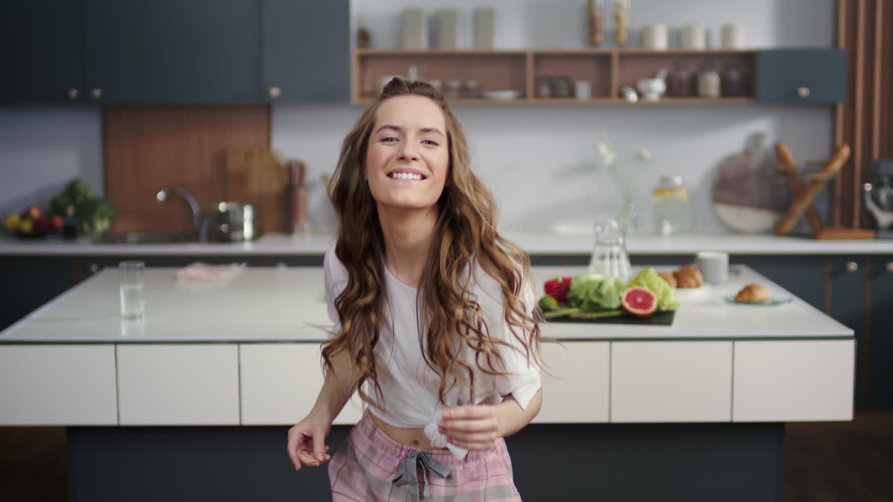 Donna energica che balla in una cucina moderna. Ragazza sorridente che schiocca le dita a casa.