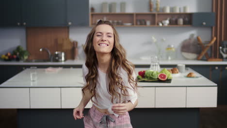 energetic woman dancing on modern kitchen. smiling girl snapping fingers at home