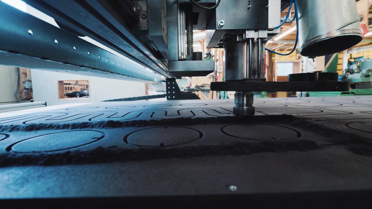 Vista em ângulo baixo de debaixo de uma máquina CNC enquanto ela corta padrões em uma chapa de madeira