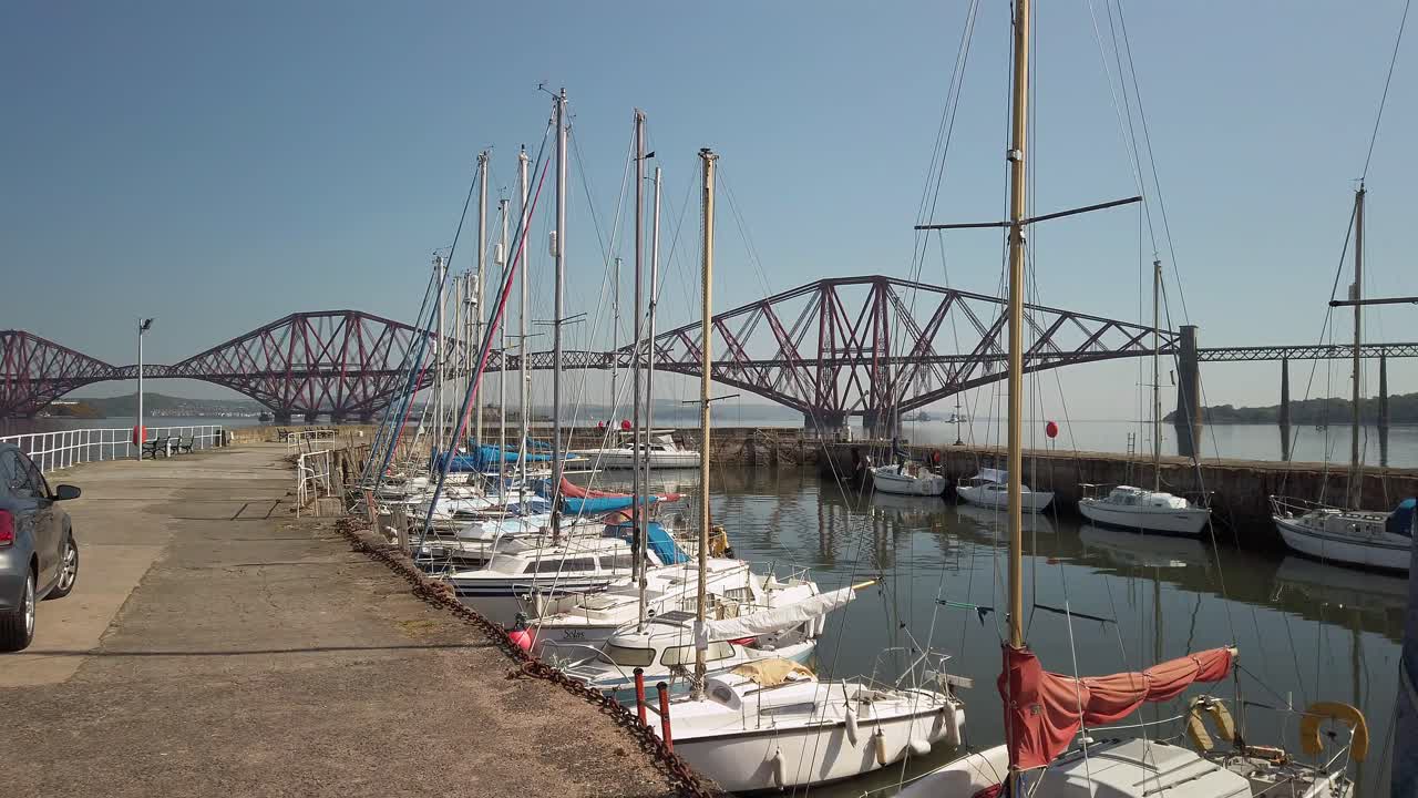 Harbor with the Forth Railway Bridge in the distance with calm water and cloudless sky