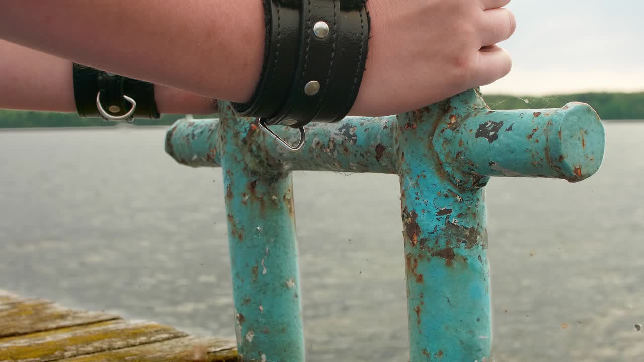 vista de las manos de la mujer con grandes pulseras negras agarrando viejo pilar oxidado en el viejo muelle de madera.