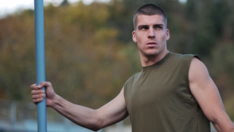 focused young athletic man recovering from workout and stretching on blue bar in training area