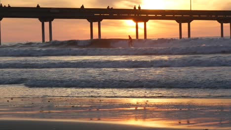 surfers surfing by pier. ocean water waves, people and sky at sunset. california