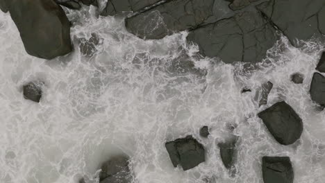 close slow motion aerial footage top down of ocean waves crashing into rocks