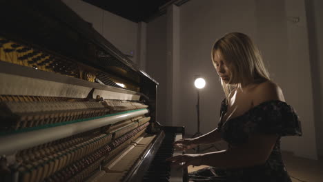 pianist playing upright piano with open sound board showing hammers striking the strings