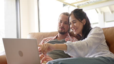 una pareja diversa se relaja con una computadora portátil en un sofá acogedor en casa