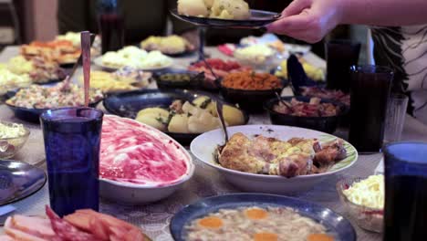 a woman puts boiled potatoes in a plate at the festive table. many dishes on the table, homemade