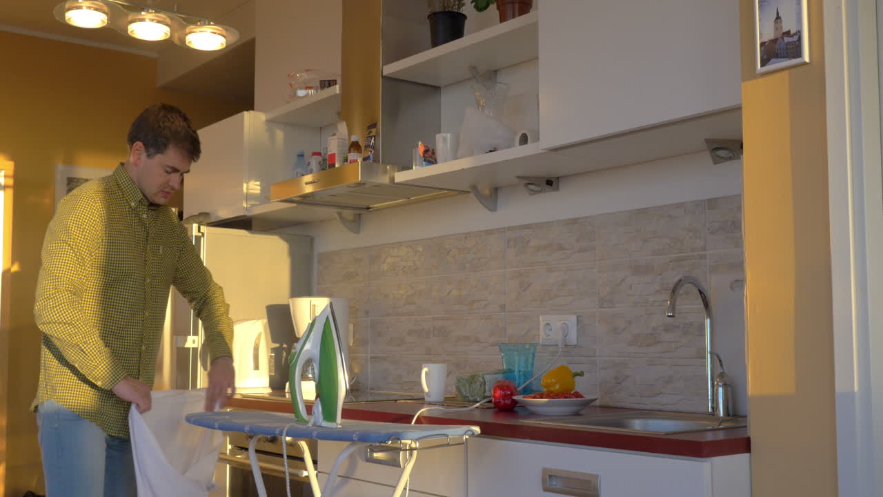 Uomo che stira una camicia bianca in cucina