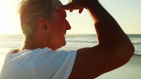 senior man shielding eyes on beach