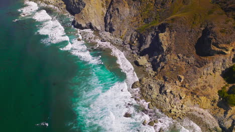Aquamarine waters of Pacific Ocean meeting rugged craggy rocks of the California coast. Amazing white waves at Morro Bay from aerial view.